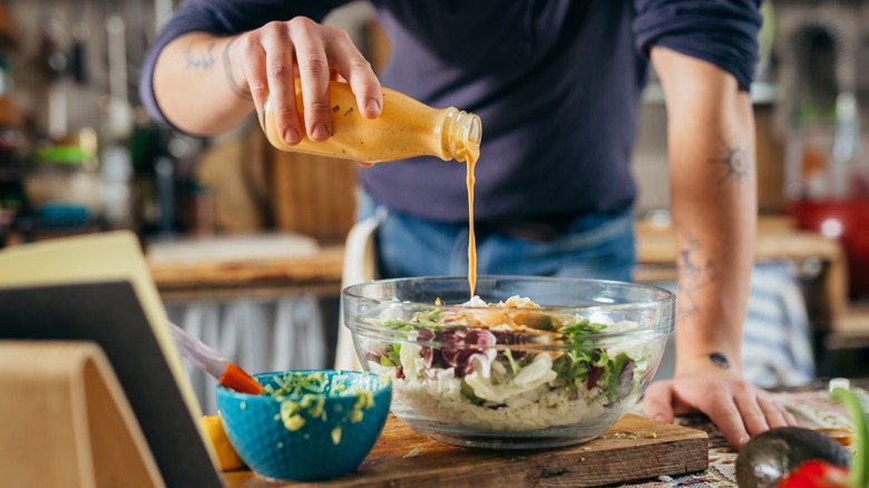 Person pouring dressing on top of salad