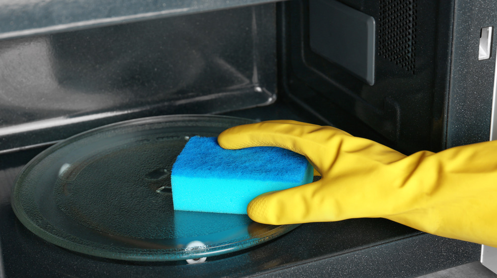 Gloved hand with sponge in microwave