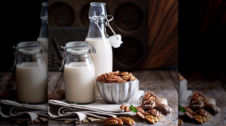 Pecan milk in glass jars next to raw pecans in metal bowl