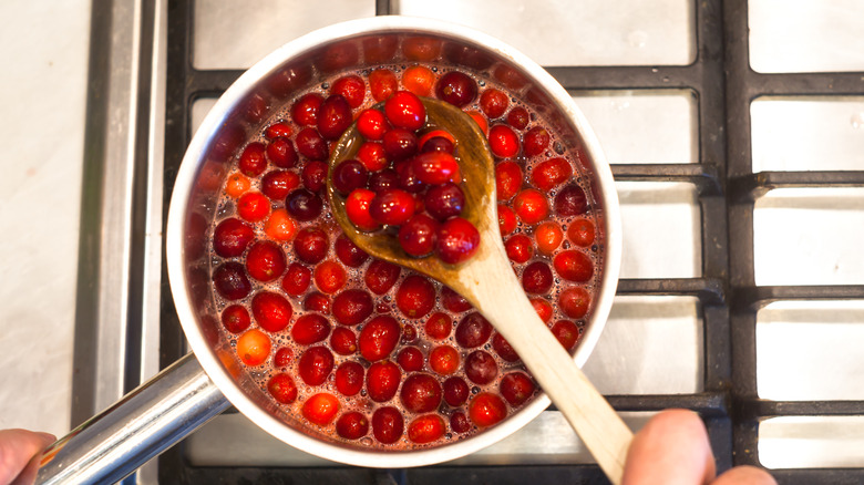 Stirring pot of boiled cranberries with wooden spoon