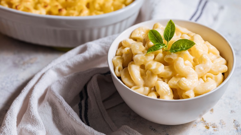 mac and cheese with basil garnish in a small white bowl next to a mac and cheese casserole 