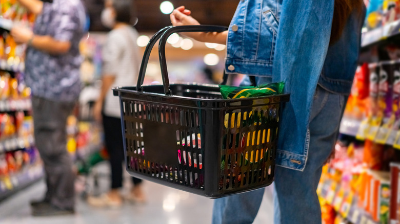 person holding black shopping basket with defocused background of grocery store