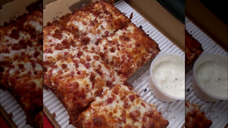 A pizza topped with bacon and a side of ranch.