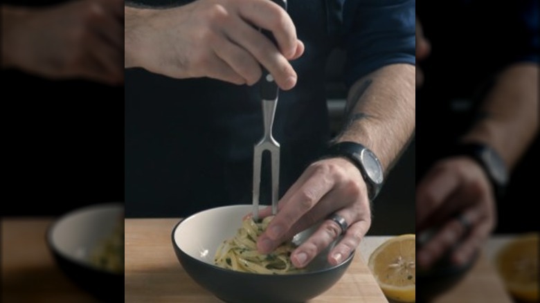 Person plating pasta with a carving fork