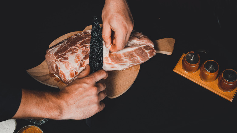 Hands trimming the fat off a piece of pork