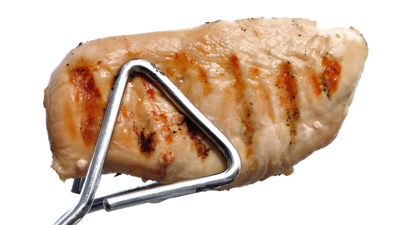 Barbecue tongs holding chicken breast