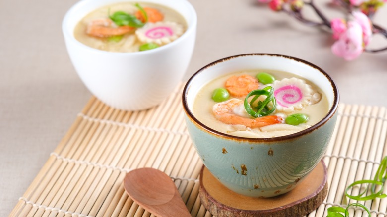 A bowl of chawanmushi with shrimp carrots and beans inside against a bamboo background