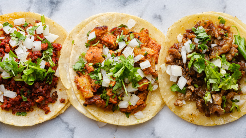 Three corn tacos filled with meat on marble slab