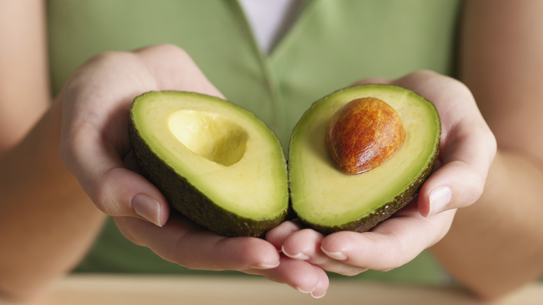 hand holding halved avocado