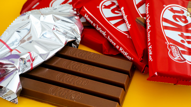 An unwrapped KitKat bar in front of a stack of chocolate bars