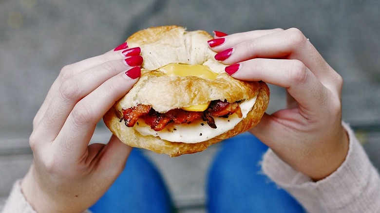 hands holding croissant bacon sandwich