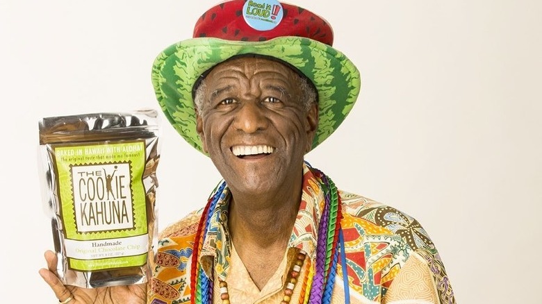 Wally Amos in colorful clothing holding bag of cookies