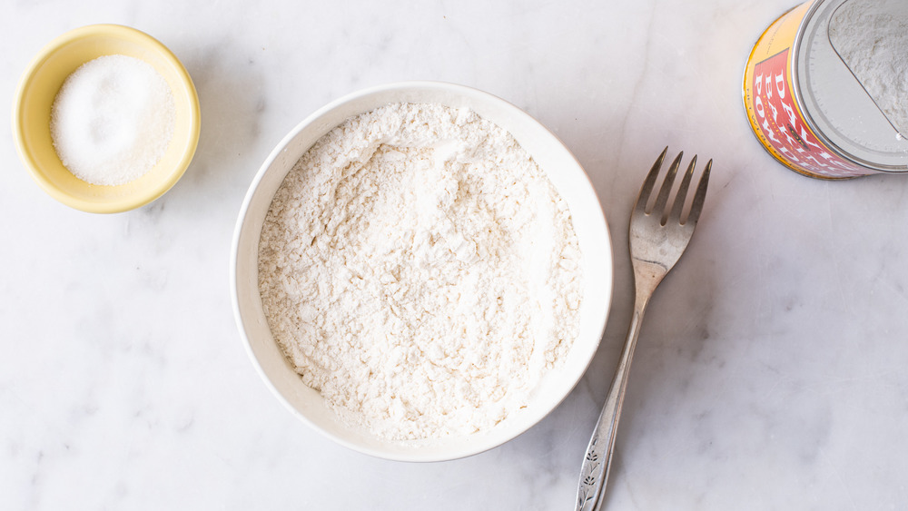 A bowl of flour next to salt and baking powder