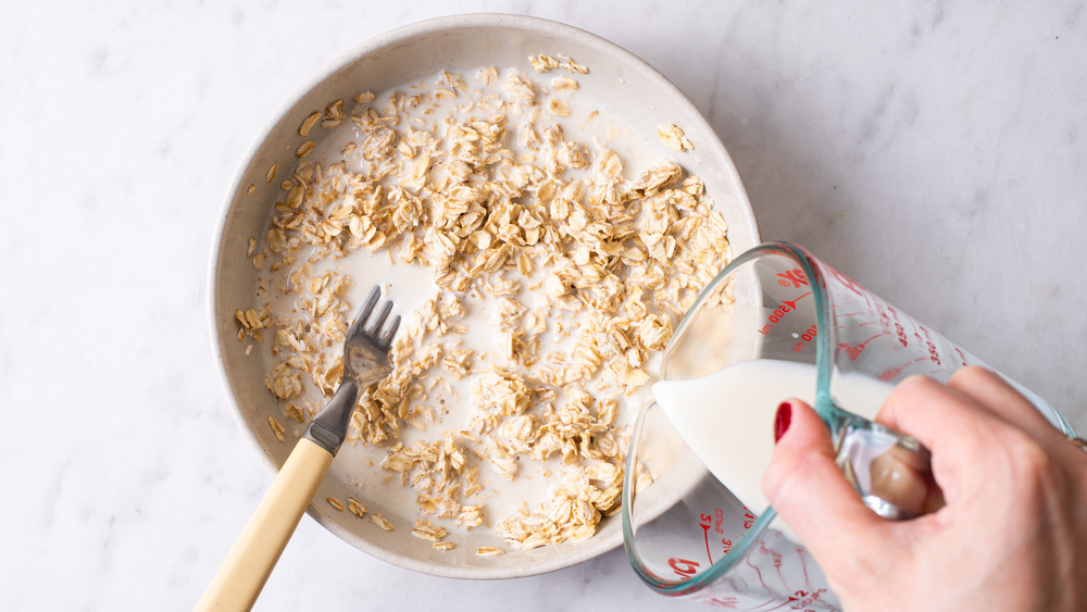 Woman's hand pouring milk into a bowl with oats