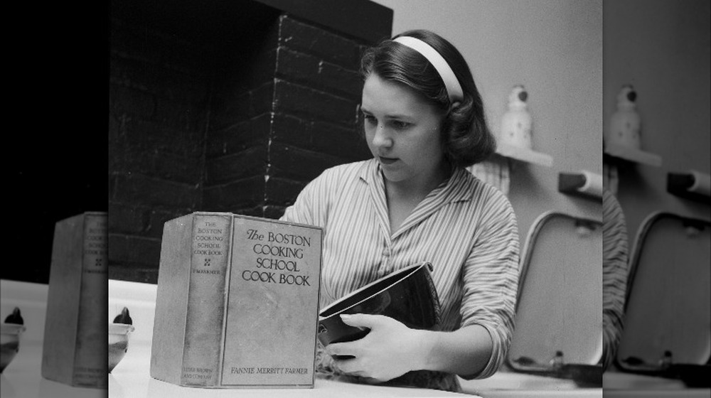 Woman reads Fannie Farmer's cookbook