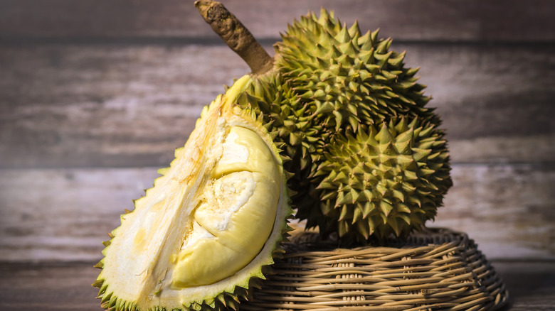 Whole durian fruit next to a halved durian