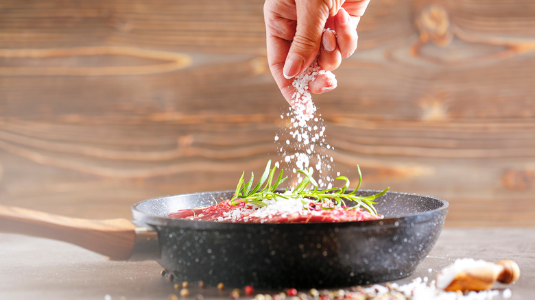 Salt sprinkled onto food in a pan