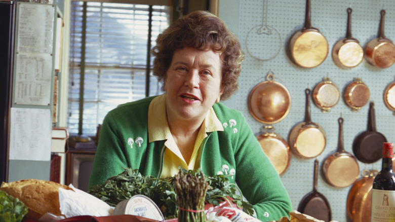 Julia Child in a green sweater with food on table.