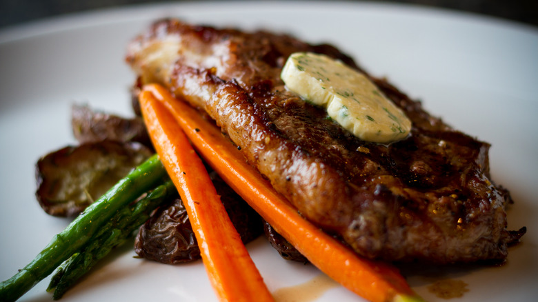steak on a plate with garlic butter, carrots, and asparagus