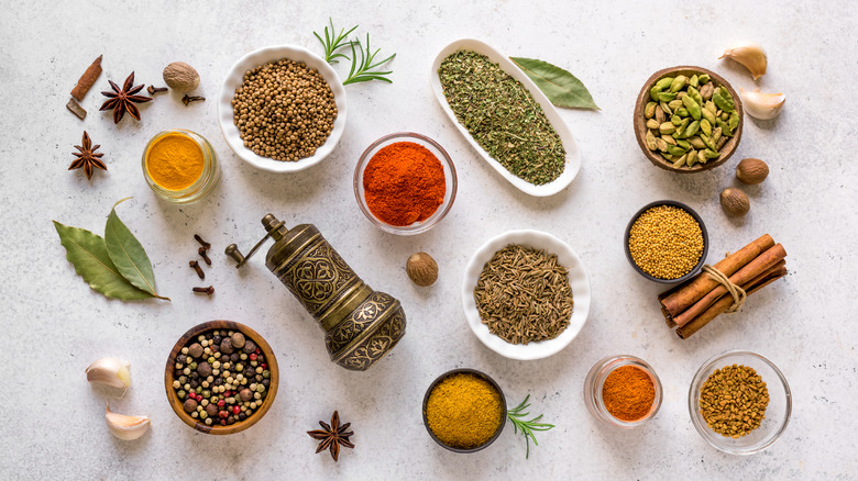 Bowls of ground and whole spices next to spice grinder