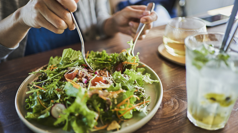 Person tossing salad on plate