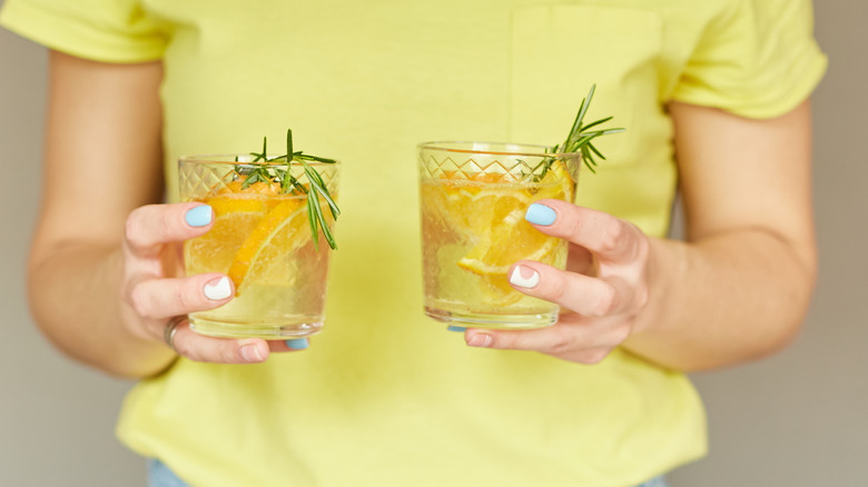 person in yellow shirt holding two glass tumblers of lemonade