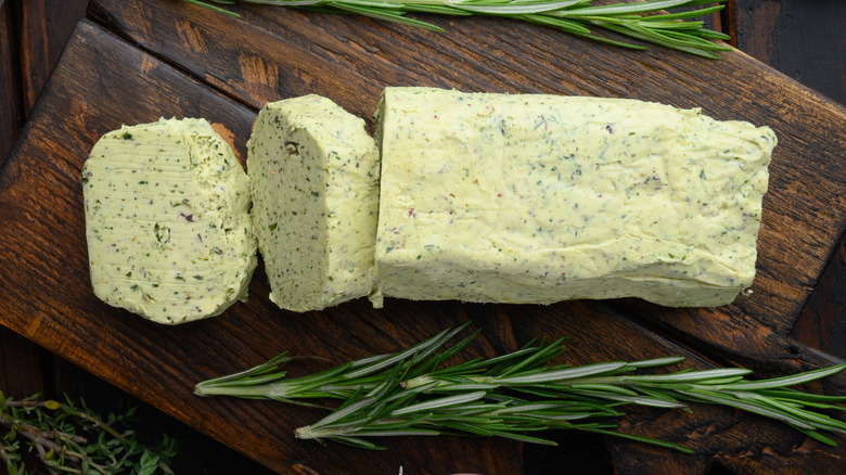 Herb butter sliced on a wooden block with rosemary sprig