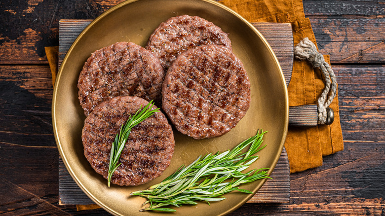 four cooked burger patties on a plate in a rustic setting