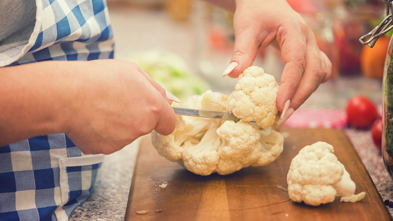 person cutting cauliflower on cutting board