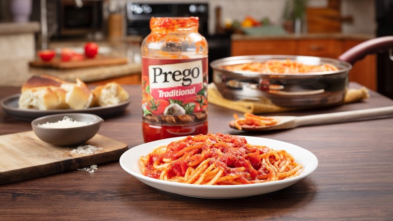 Open jar of Prego traditional sauce next to plate of spaghetti