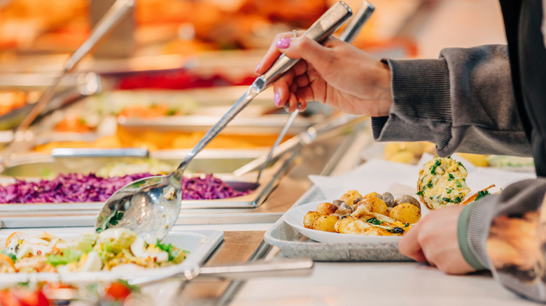 woman serving herself food at a buffet restaurant