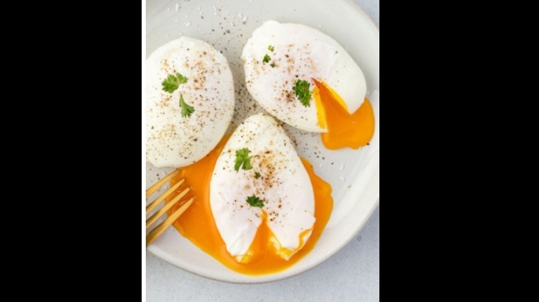 Three poached eggs cut in the middle with the yolk running, topped with salt, pepper and parsley 