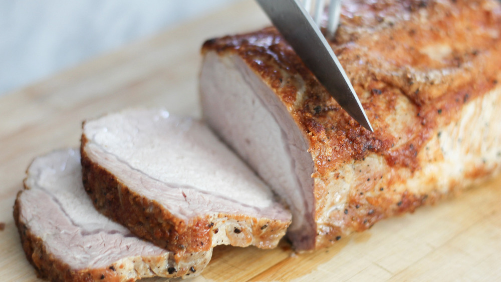 Knife slicing cooked pork loin recipe