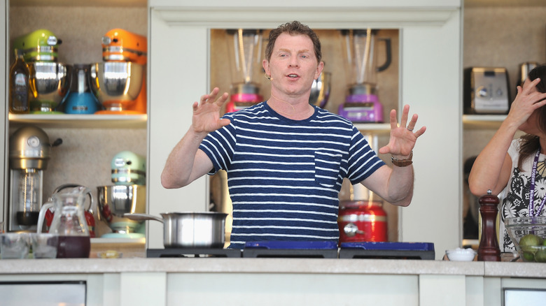 Bobby Flay in a striped shirt speaking in a kitchen