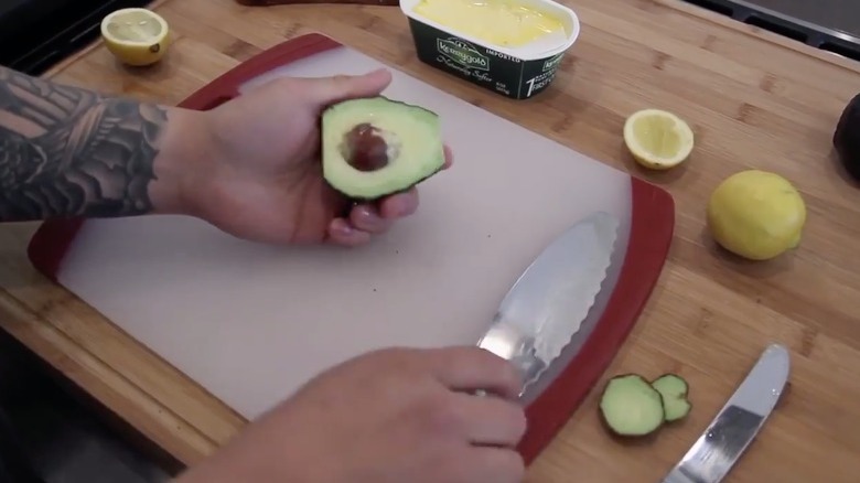 Hand holding an avocado with a knife