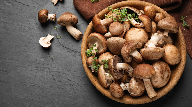 Wooden bowl full of mushrooms on gray slab