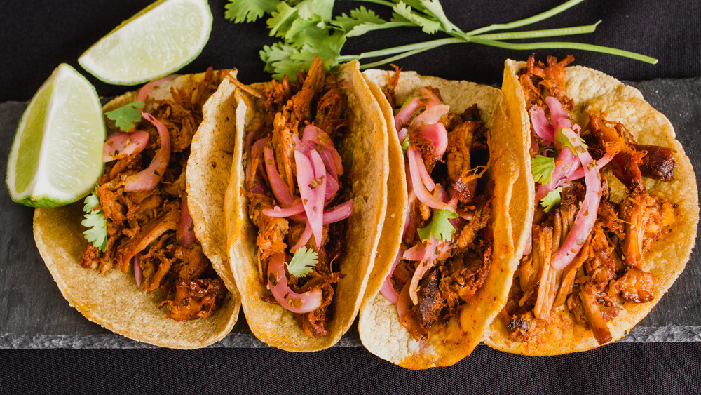 four tacos on black background with lime wedges