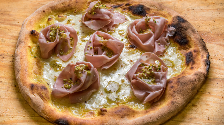 Mortadella pistachio pizza on wooden surface