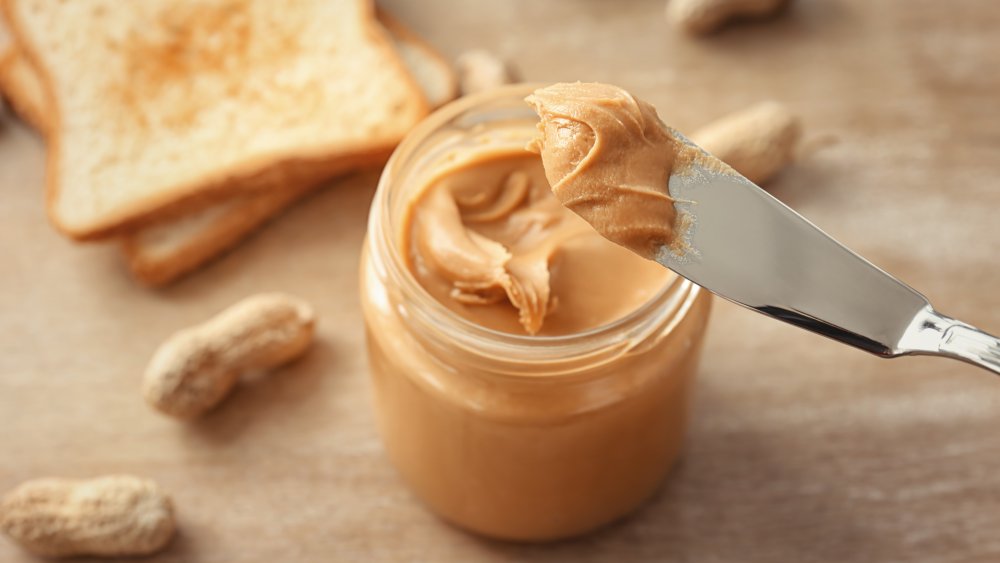 knife with creamy peanut butter on table next to toast and whole peanuts