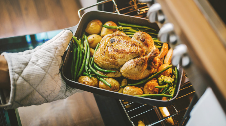 Roast chicken and vegetables being pulled from the overn