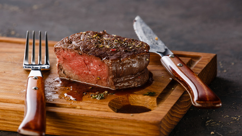 Piece of rare steak on wooden board with fork and knife