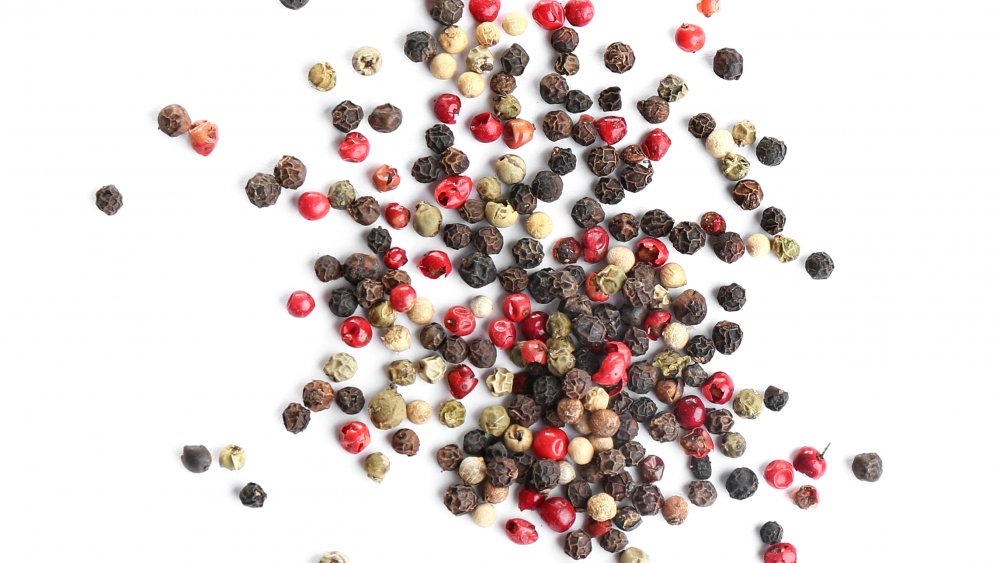 Mixed whole white, green, black, and red peppercorns on a white background.