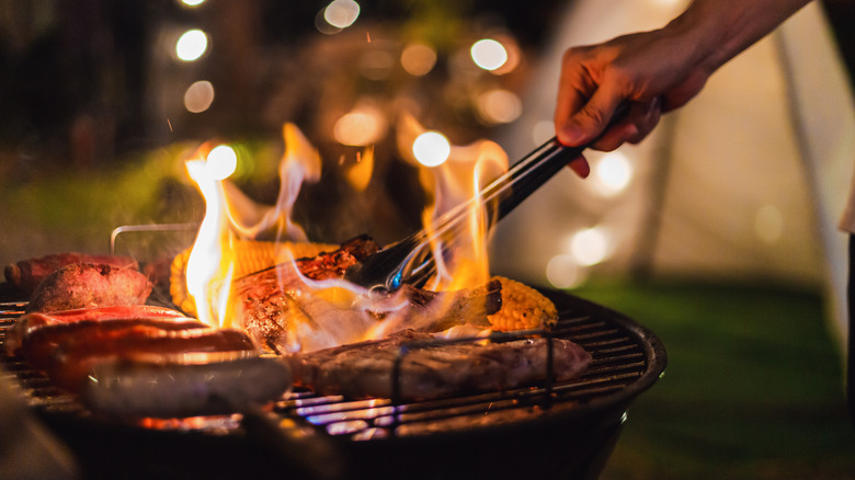 Tongs grabbing meat from grill with flames