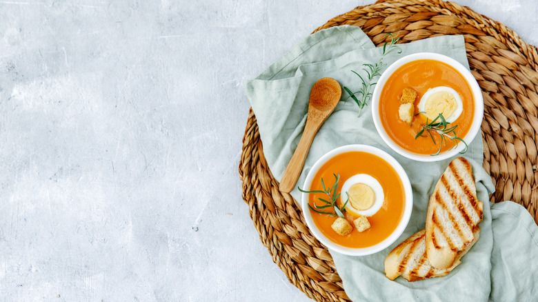 Two cups of salmorejo with hard boiled eggs, croutons and thymes on top, with slices of bread