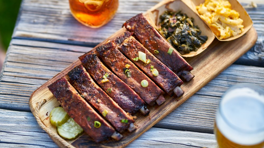 Cooked St. Louis style ribs on a wooden rectangular plate with sides of collard greens and macaroni and cheese.