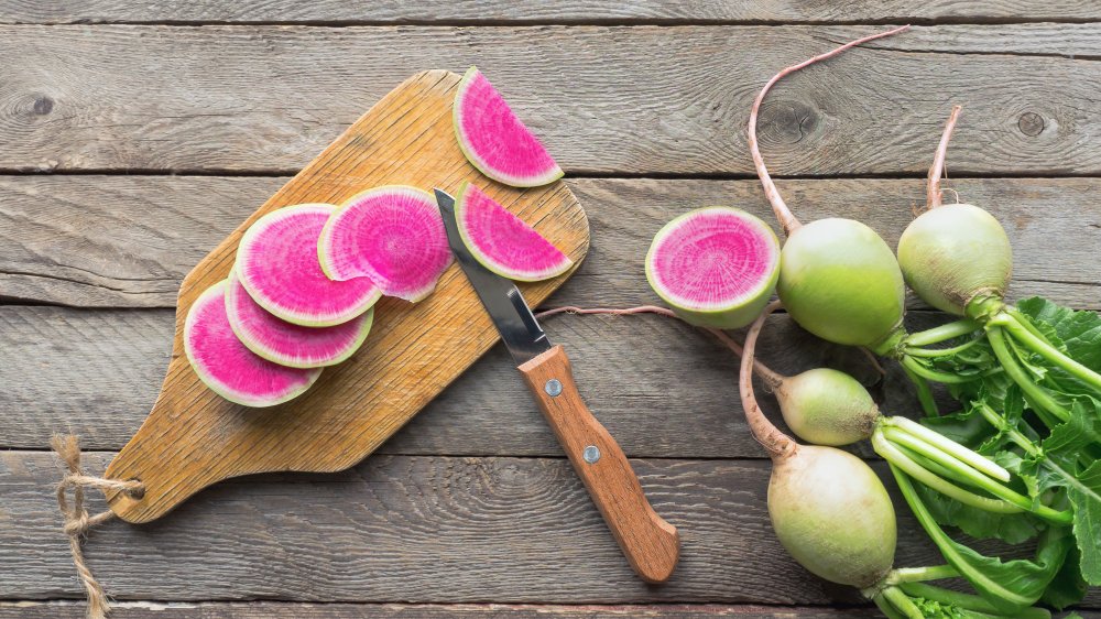 Watermelon radish slices on a wooden cutting board with whole radishes