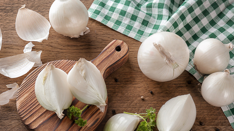 Whole and sliced white onions on a wood surface