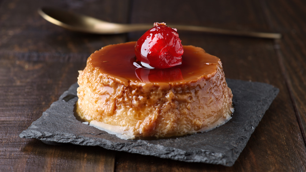 Egg custard topped with caramel and cherry on slate and spoon on wooden table