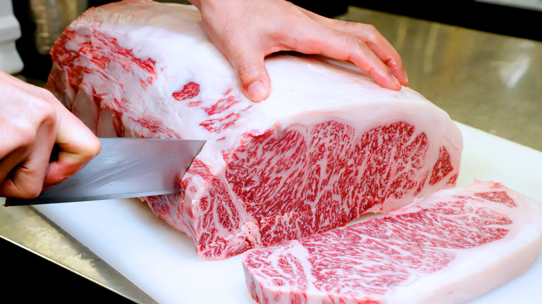 Slab of raw wagyu beef being cut on butcher block 