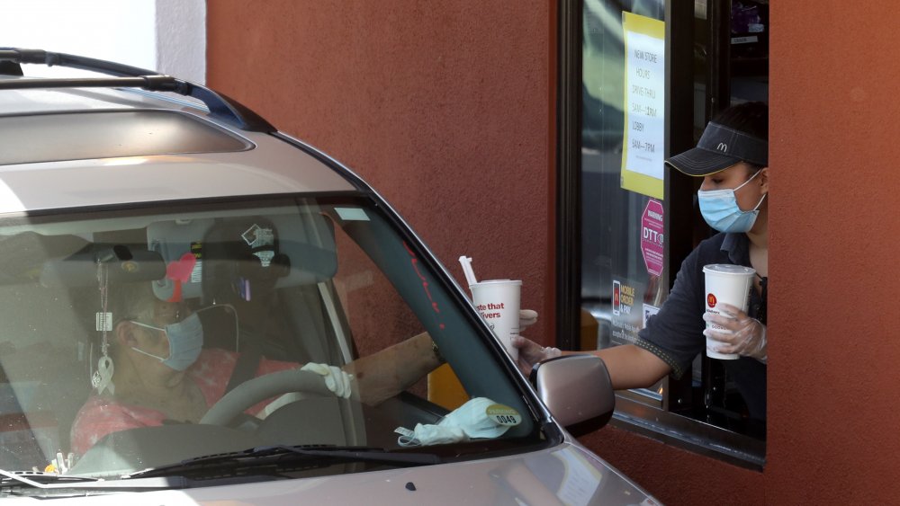 McDonald's employee with mask and gloves serves customer in drive-thru